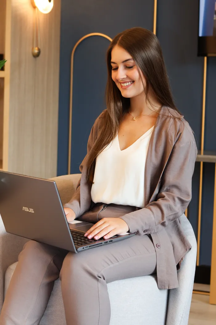 Letícia Cardoso sentada em poltrona, com o notebook no colo, sorriso solto