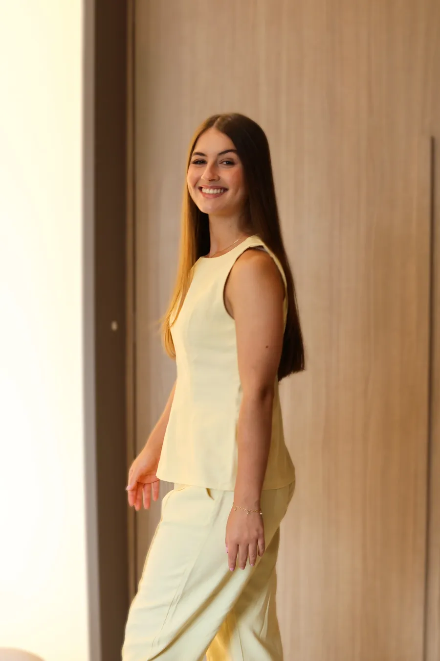 Letícia Cardoso caminhando de lado, sorrindo, com roupa amarela clara